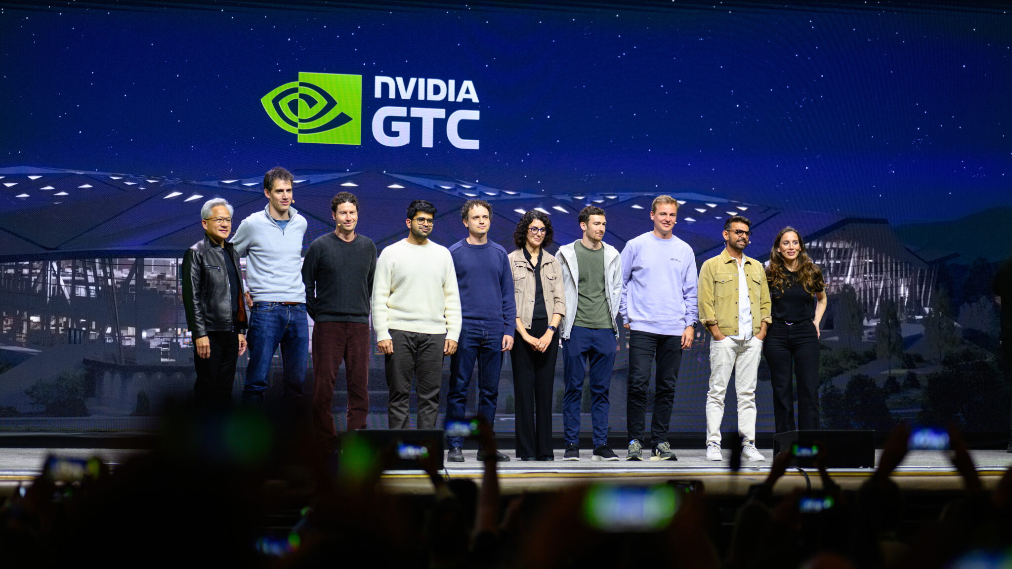 NVIDIA GTC 행사장에서 젠슨 황 CEO와 여러 AI 리더들이 무대 위에 함께 서 있는 모습이다.